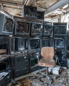 an old chair sitting in front of televisions that have been destroyed and are stacked on top of each other