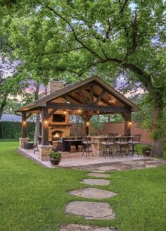 an outdoor kitchen and grill area in the middle of a yard with grass, trees, and