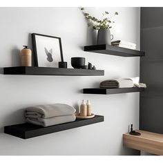 two black floating shelves in a bathroom with towels and other items on the ledges