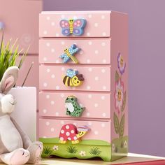 a toy rabbit sitting next to a pink dresser with magnets on it's drawers