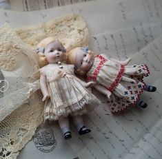 two dolls laying next to each other on lace