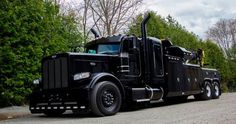 a large black truck parked on the side of a road next to trees and bushes