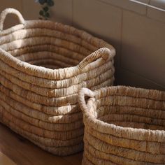 two woven baskets sitting next to each other on a wooden floor in front of a window