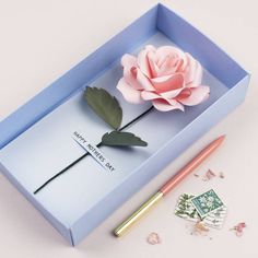 a pink rose sitting on top of a blue box next to a pen and envelope