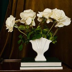 three white roses in a vase on top of a book