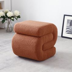 an orange ottoman sitting on top of a white floor next to a vase with flowers