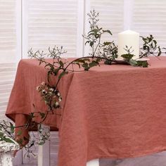 the table is covered with an orange linen and has greenery on it, along with a white candle