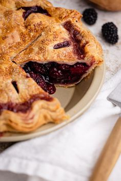 there is a pie on the plate with blackberries next to it and a knife