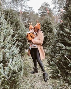 a woman holding a baby in her arms while standing between two rows of christmas trees