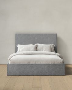 a bed sitting on top of a hard wood floor next to a white wall with pillows