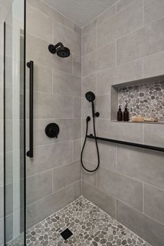 A transitional shower design with river rock floor and large format grey tile on the walls. Matte black fixtures.