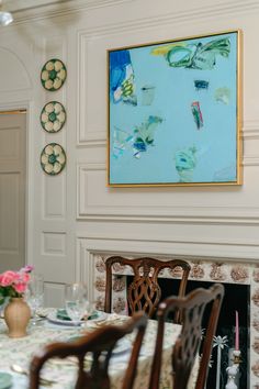 a dining room table and chairs in front of a painting on the wall above it