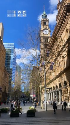 an old building with a clock tower in the center and people walking around it on a sunny day