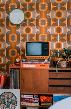 an old tv sitting on top of a dresser next to a wallpapered wall