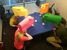 three people sitting at a table with paper hats on their heads and balls in the air