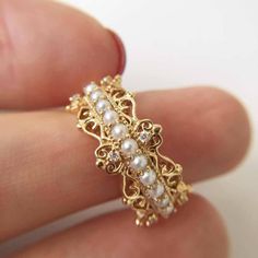 a close up of a person's hand holding a ring with pearls on it