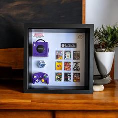 there is a framed photo with video game memorabilia on the table next to a potted plant