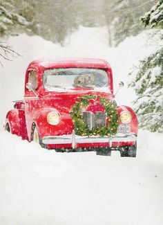 an old red truck with a wreath on the front driving down a snow covered road