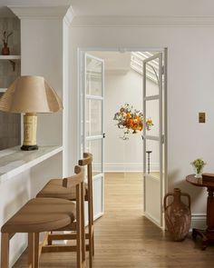 an open door leading into a white room with wooden chairs and vases on the table