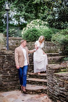 a man and woman standing on steps in the park holding each other's hands