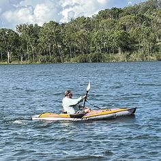 a man in a kayak paddling on the water with trees in the background