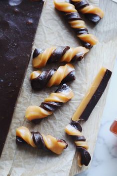 chocolate and caramel pretzels are arranged on wax paper next to a bar of dark chocolate