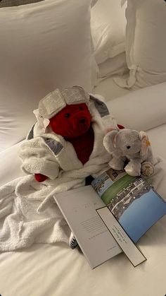 a stuffed animal is sitting next to a book on a bed with white sheets and pillows