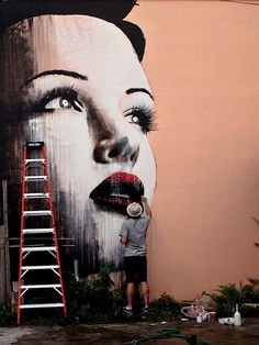 a man standing next to a giant painting of a woman's face on the side of a building