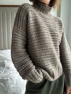 a woman standing in front of a bed wearing a sweater