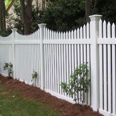 a white picket fence in front of a house with trees on the side and bushes growing between it