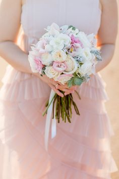 a woman in a pink dress holding a bouquet of white and pink flowers on her wedding day