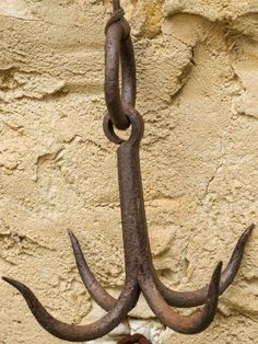 an anchor hanging on the side of a stone wall with rusted metal hooks