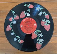 a record with strawberries painted on it sitting on a wooden floor next to a wall