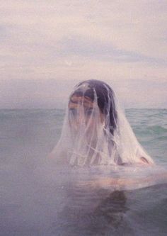 black and white photograph of a woman in the ocean with veil over her head looking out to sea