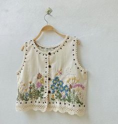 a white top with flowers on it hanging from a wall next to a wooden hanger