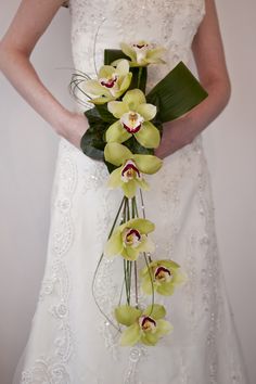 a woman in a wedding dress holding a bouquet of green orchids and greenery