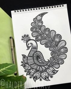 a drawing of a peacock on paper next to a pen and some green leafy plants