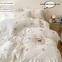 a bed with white comforters and pink flowers on it, next to a night stand