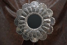 a silver flower shaped mirror sitting on top of a brown cloth covered table next to a wall