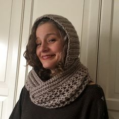 a smiling woman wearing a knitted cowl scarf and hood in front of a white door