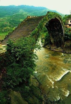 an old bridge over a river surrounded by mountains