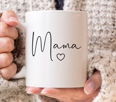 a woman holding a white coffee mug with the word mama written in cursive font