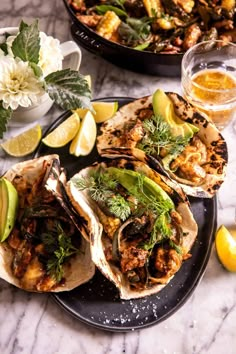 three tacos on a plate with limes and other food items next to them