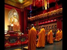 several monks in orange robes stand at the front of a room with red walls and gold decorations