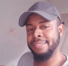 a close up of a person wearing a hat and smiling at the camera with a white wall in the background