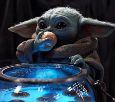 the baby yoda is sitting on top of a blue glass bowl with something in it's mouth