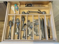 a drawer filled with silverware and utensils on top of a wooden table