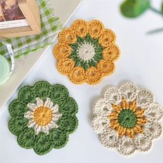 three crocheted flower coasters sitting on top of a white table next to a book