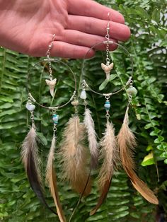 a hand holding a pair of hoop earrings with feathers hanging from it