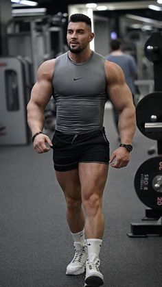 a man in grey shirt and black shorts standing next to a barbell